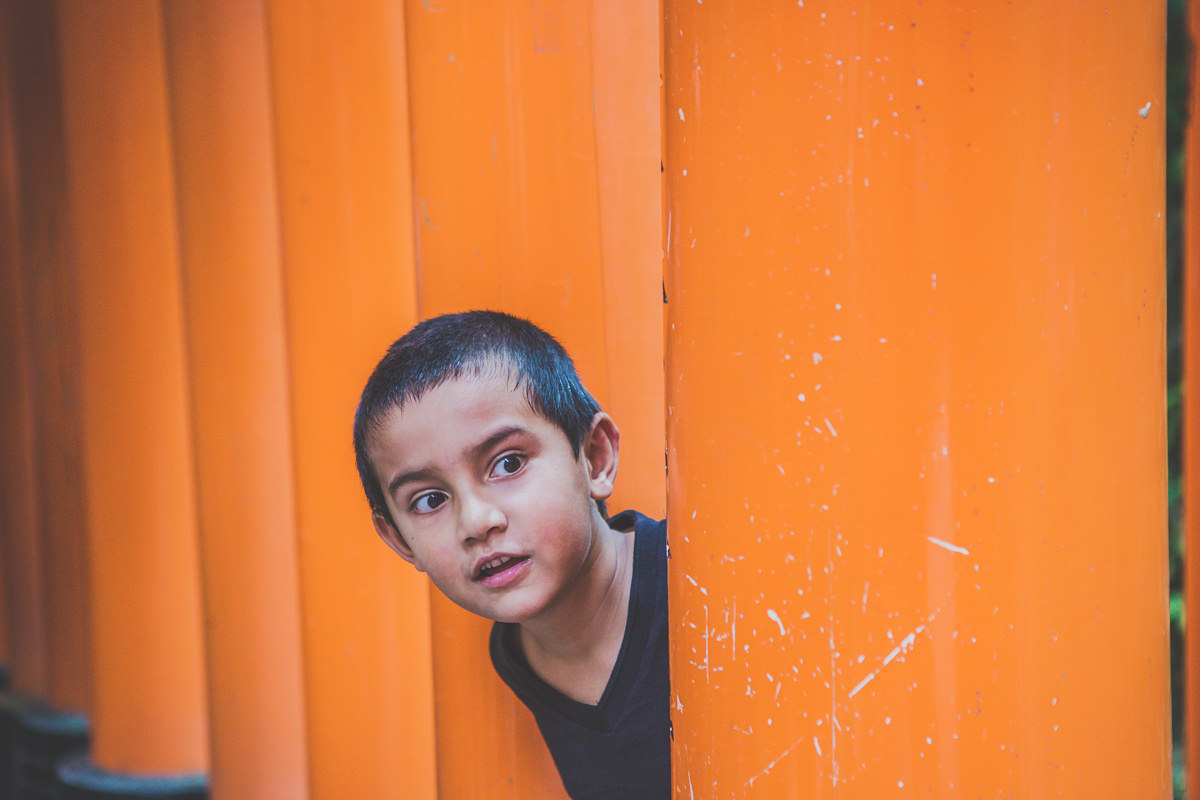 little boy peeking out of the red gates in kyoto - kids photography