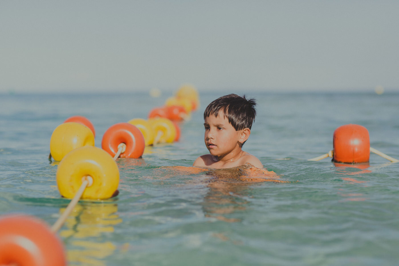 boy swimming in the ocean with colourful (yellow and red) buoys